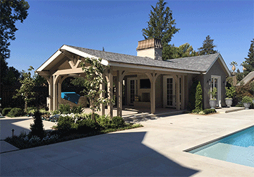 Late-afternoon backyard view of a poolhouse and portico with detailed architectural features