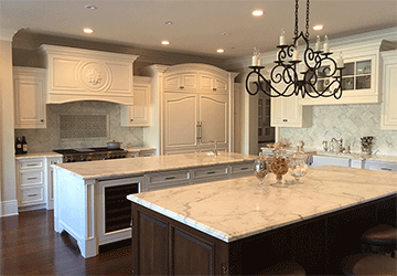Angled view of a spacious kitchen with a hardwood floor, white marble countertops, detailed white cabinetry, and a wrought-iron chandelier