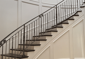 Full view of a majestic hardwood curving staircase with detailed scrollwork on the dark bannisters and paneled white walls